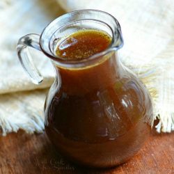 close up view from above of syrup jar filled with homemade pumpkin syrup on a wooden table with a white cloth in the background