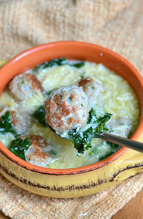 Italian Wedding Soup with Turkey Meatballs and Orzo in a yellow bowl. Spoon that's above the bowl holds a meatball and piece of green kale.