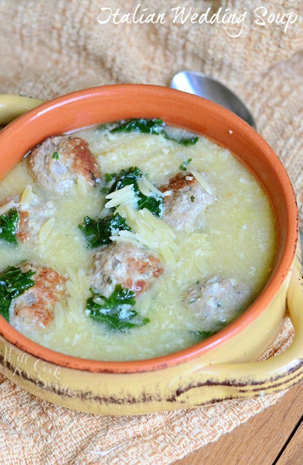 Italian Wedding Soup with Turkey Meatballs and Orzo in a bowl with a spoon next to it on a table with a brown kitchen towel 