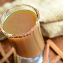 close up view from above of dessert coffee mug filled with light spiced pimpkin after dinner coffee on a wood table with cinnamon sprigs and a brown cloth around the base of glass