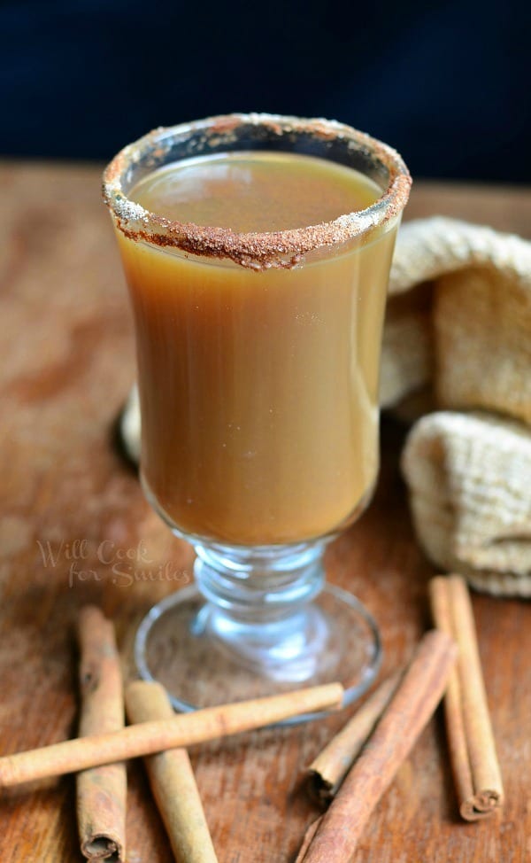 Spiced Pumpkin Coffee in a glass with cinnamon around the edge of the glass and cinnamon sticks around the bottom on a wood table 