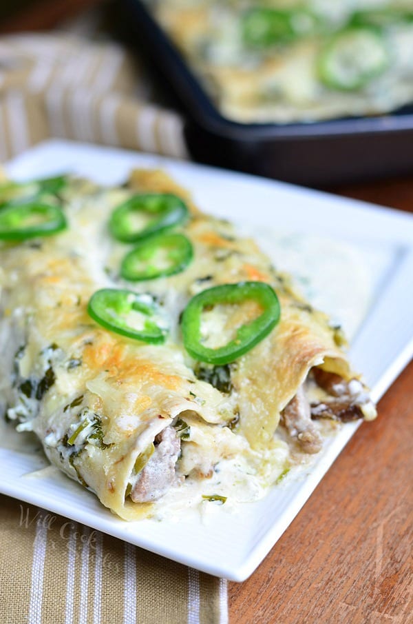 Steak Enchiladas with Jalapeño Cilantro Cream Sauce on top with sliced jalapenos on a white plate 