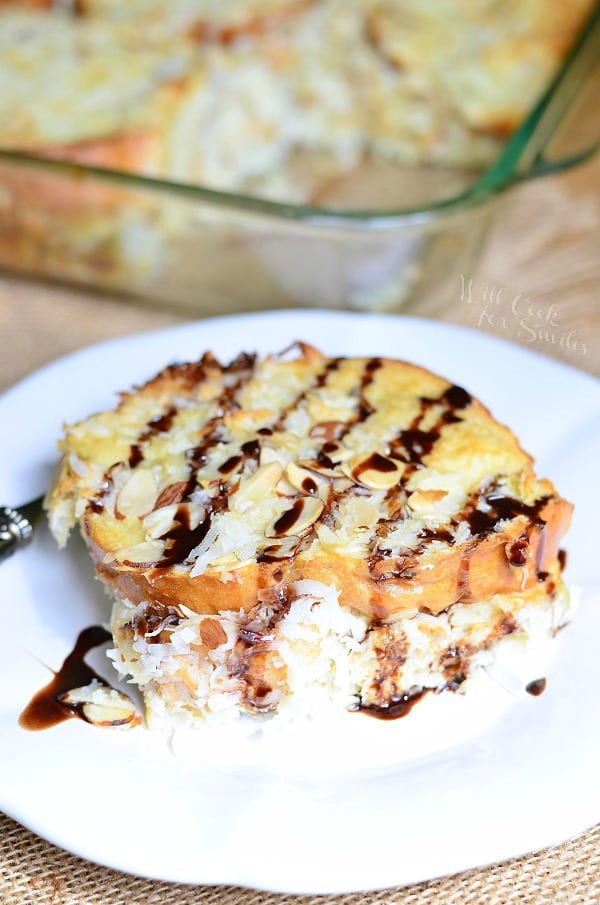 one portion of almond joy french toast bake on a round white plate on tan placemat with baking dish and rest of bake in background