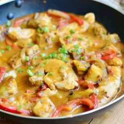 close up view of saute pan with easy thei coconut curry chicken and vegetables on a wood table with tan striped cloth in background behind pan