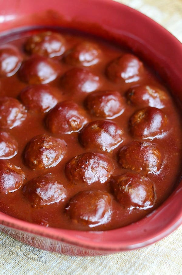 Red ceramic baking dish filled with cooked meatballs in sauce on a tan placemat