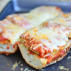 close up view of open faced baked eggplant parmesan sub on a baking pan on tan placemat on wood table