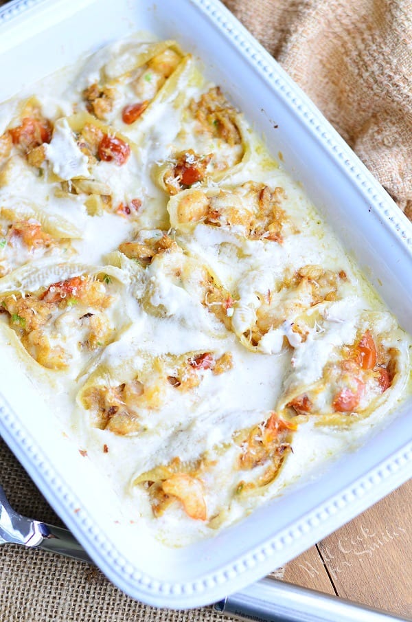 Seafood Alfredo Stuffed Shells are served in a white casserole dish. The white Alfredo sauce covers the pasta well. 