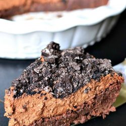 white baking dish with brownie bottom chocolate mousse pie on a black table with a silver cake cutter with 1 slice of pie in foreground