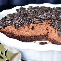 close up view of white baking dish with brownie bottom chocolate mousse pie on a black table with a silver cake cutter in foreground