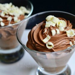 close up view of dessert glass filled with chocolate mousse on a white rectangular plate with additional glass and mousse in background