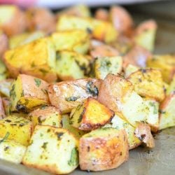 close up view of oven roasted potatoes cooked on a metal sheet tray presented on a wooden table with a white cloth with red stripes in background