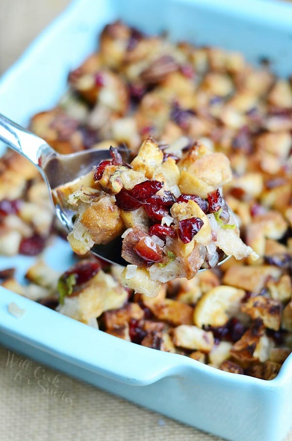 Cranberry Stuffing with Pecans in a casserole dish with a spoon lifting some out 