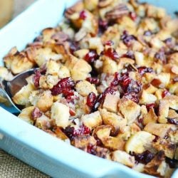 serving spoon in a Blue baking dish with cranberry pecan stuffing on a tan placemat
