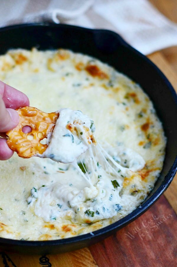 dipping pretzel into Four Cheese Hot Dip that is in a cast iron pan 