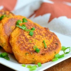 close up view of 4 sweet potato cakes shingled in a line on a white plate garnished with scallions. White plate sits on a wooden table with a red and white cloth in the background