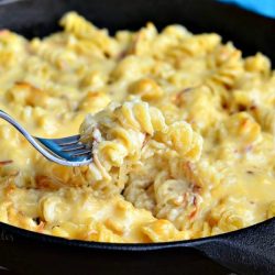black skillet filled with caramelized onion gouda macaroni and cheese on a wooden table and blue cloth with a fork pulling out one bite
