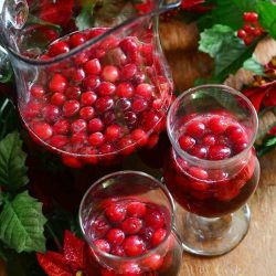 view from above of 2 wine glasses filled with cranberry sangria on a wooden table in front of a pitcher filled with additional sangria and winter floral decor on table with around the glasses.