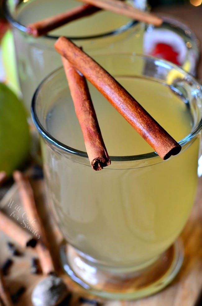 Green Apple Cider in a clear glass with cinnamon sticks over the top 