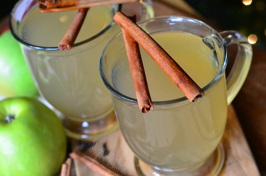 Green Apple Cider in a clear glass with cinnamon sticks over the top 