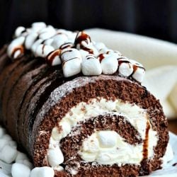 white rectangular plate with a whole hot chocolate cake roll on a wooden table with a white cloth in background