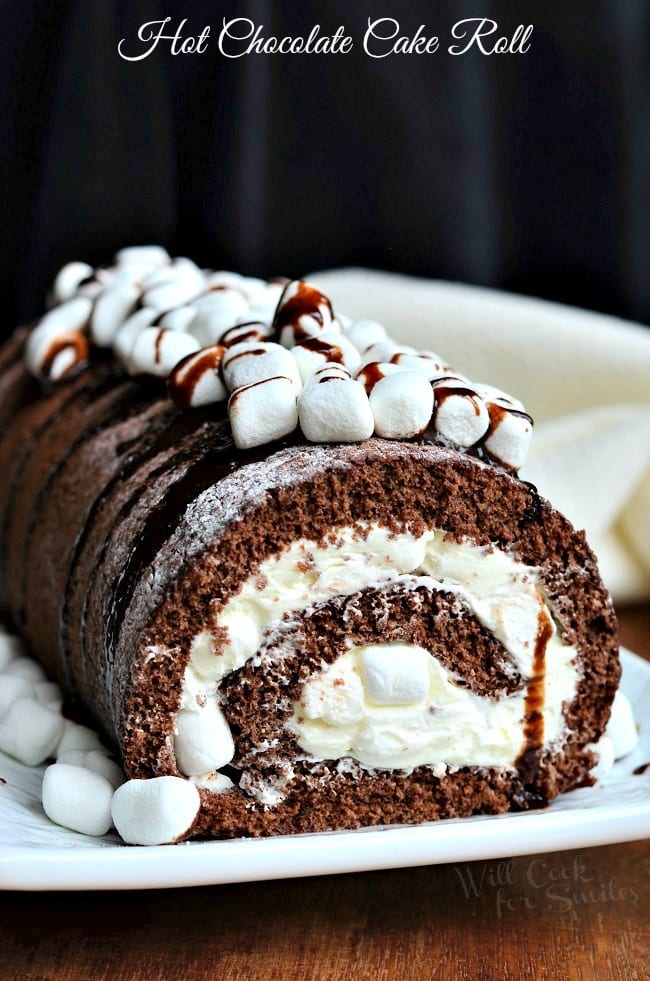 Hot Chocolate Cake Roll with cream in the middle of the cake roll and chocolate sauce and mini marshmallows on top of the cake 