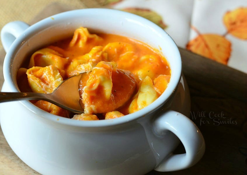 Roasted Bell Pepper Tortellini Soup in a white soup bowl with a spoon lifting out some 