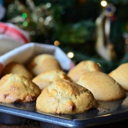 muffin baking pan with white chcolage chip eggnog muffins on a wooden table in front of a christmas tree and a white and red cloth