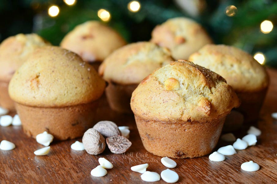 White Chocolate Chip Eggnog Muffins on a table with white chocolate chips and whole nutmeg