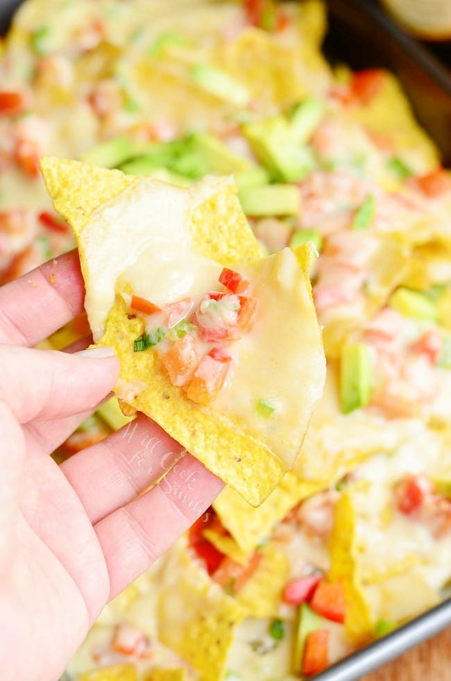 lifting a Nachos with Veggies and Cheese Sauce over it with tomato and avocado 