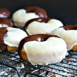 close up view of Black and white glazed donuts on a cooling rack on a black table with powdered sugar on table