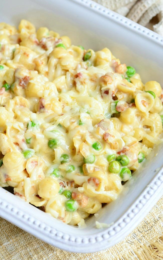 Creamy White Macaroni & Cheese with Peas Onions & Bacon in a white casserole dish 