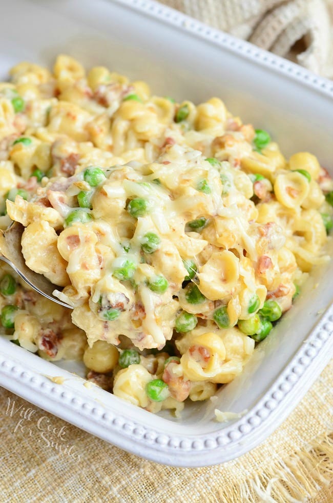 Creamy White Macaroni & Cheese with Peas Onions & Bacon in a white baking dish 