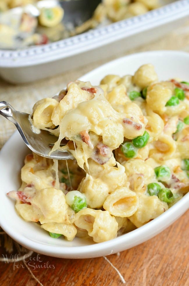 Creamy White Macaroni & Cheese with Peas Onions & Bacon in a bowl with a fork scooping some up 