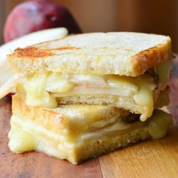 view from the front of a dijon havarti pear grilled cheese sandwich cut in half with the 2 halves stacked on each other on a wood table with a pear in the background