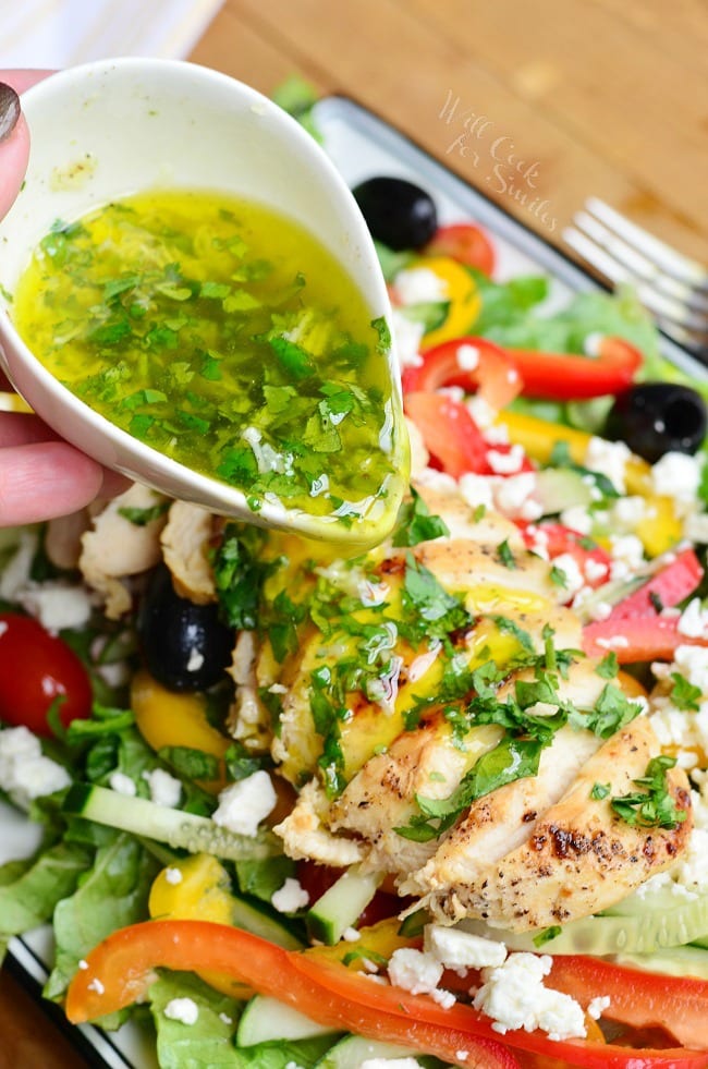 pouring lemon herb vinaigrette over the chicken on the salad