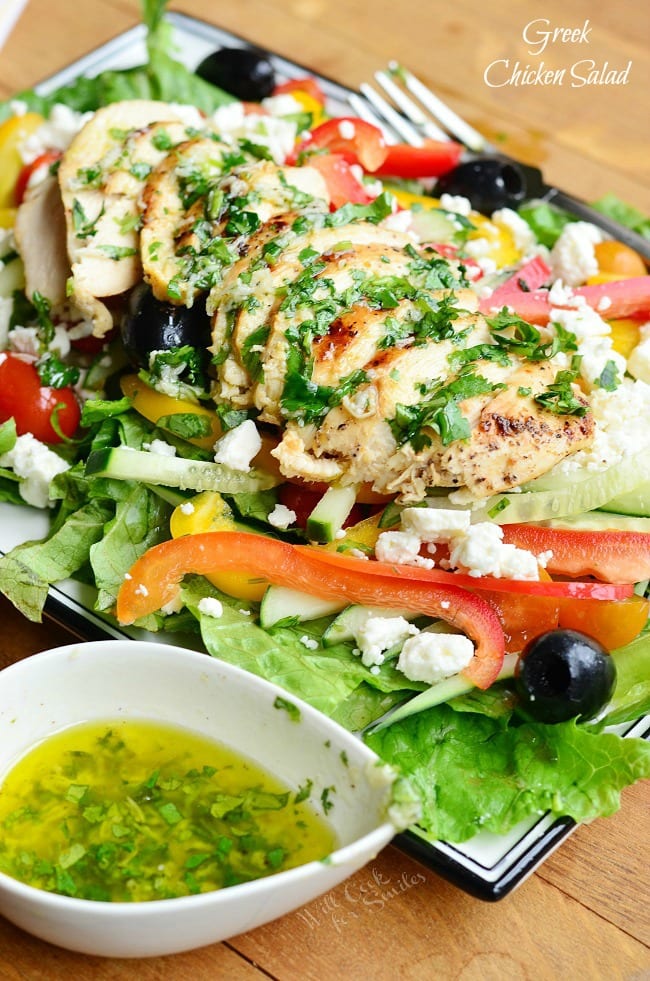 greek chicken salad on a plate with red peppers, banana peppers, black olives, and feta cheese with a side of dressing in a bowl 