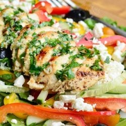 close up view of white rectangular plate with a black rim whit greek chicken salad on a wooden table