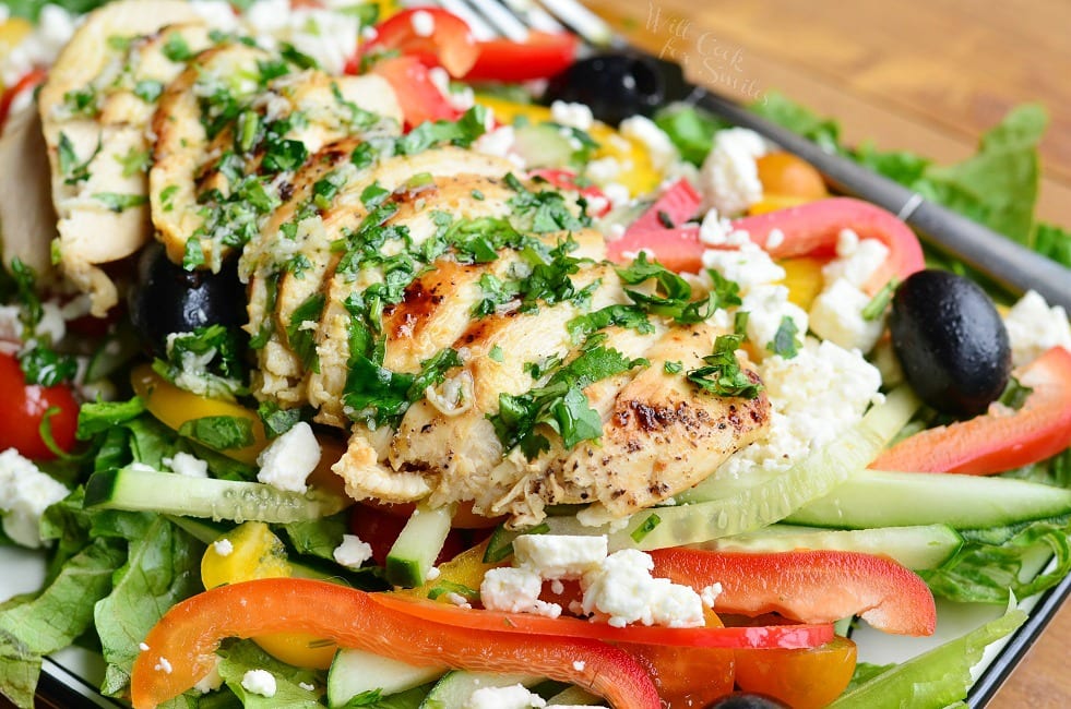 horizontal image on sliced chicken on top of salad with sliced bell peppers around and feta and black olives