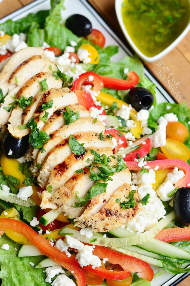 sliced chicken bread on top of a Greek salad with dressing next to the plate