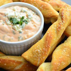 white crock filled with creamy buffalo dipping sauce surounded by homemade soft pretzel twists viewed close up and slight above the twists