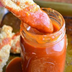 Chicken strip being dipped into homemade whiskey BBQ sauce in a mason jar