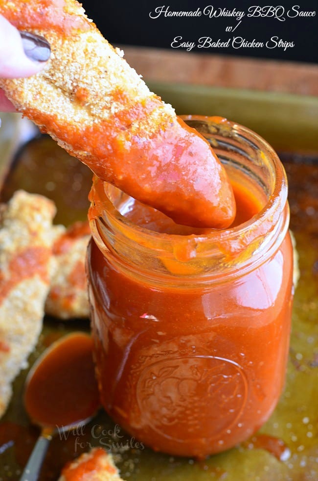 Chicken strip being dipped into homemade whiskey BBQ sauce in a mason jar