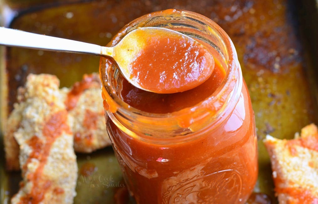 Whiskey BBQ Sauce in a mason jar with a spoon scooping some out, Chicken Strips on a baking sheet 