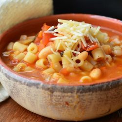 soup crock filled with pasta E fagioli soup on a wooden table with a white cloth to the side of the bowl