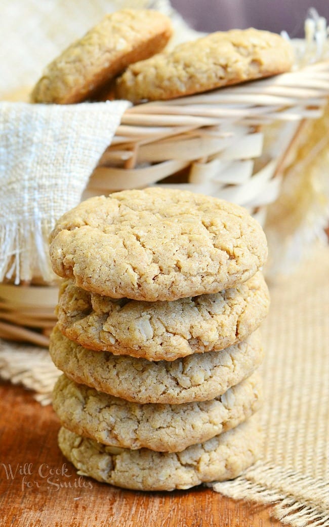 Soft Almond Butter Oatmeal Cookies stacked up on a table with a basket in the background with cookies in it  