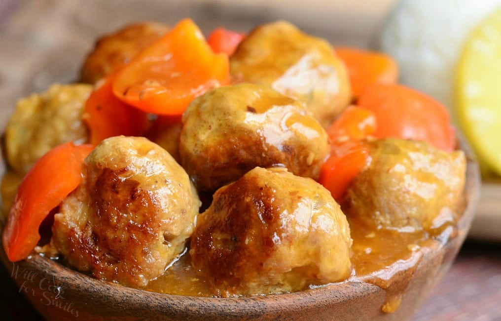 wooden bowl over flowing with sweet and sour turkey meatballs topped with peppers on a wooden table