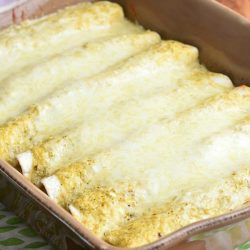 Brown baking dish filled with portions of beef enchiladas on a green and white cloth on a wooden table.