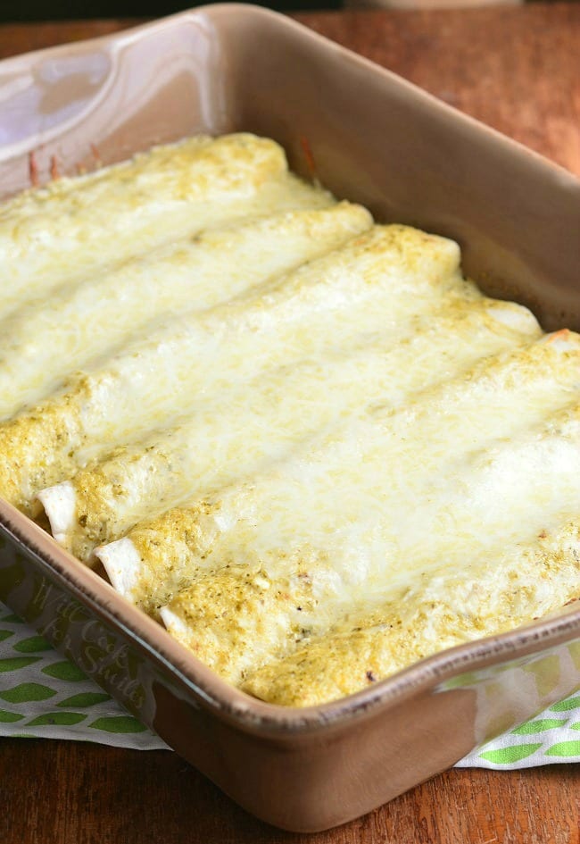 Brown baking dish filled with portions of beef enchiladas on a green and white cloth on a wooden table.