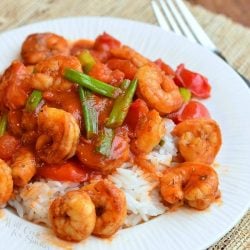 Cajun shrimp rice entree on a white round plate sitting on a tan placemat and a fork below the plate to the right all viewed from above.