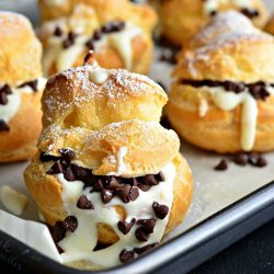 close up view of a Baking pan with wax paper holding cannoli pastry cream puffs on a black table